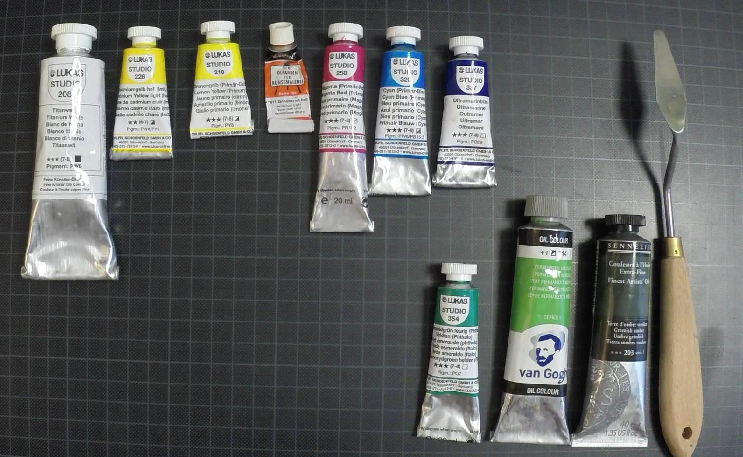 Farbtuben auf einer Schneideunterlage, doppelter Farbkreis plus Titanweiss und drei Grüntöne dazu